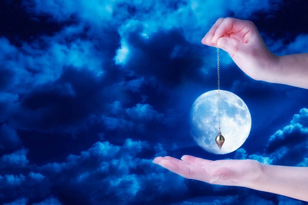 hands holding a pendulum in front of the moon